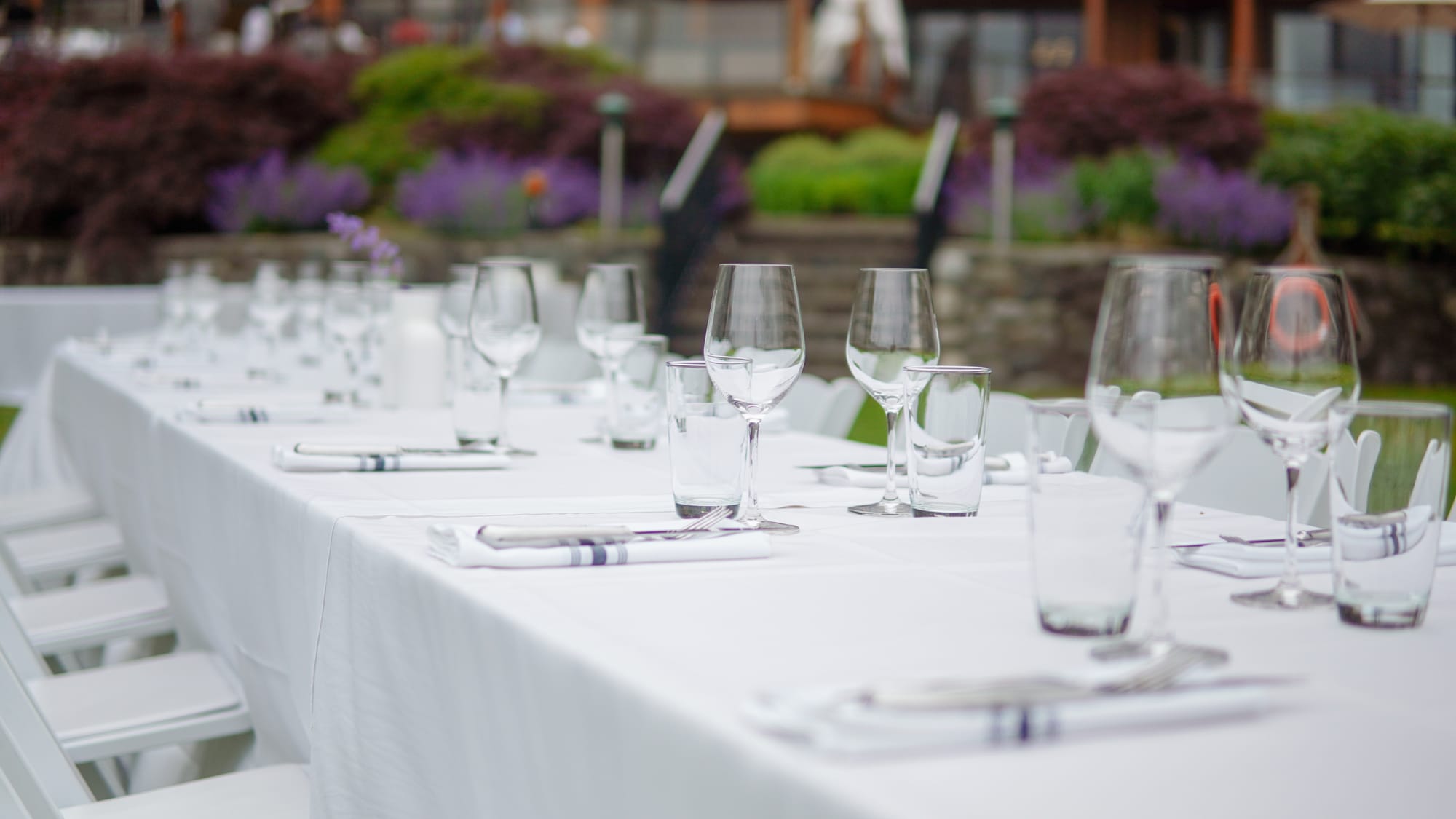 A long catered dinner table set for the group, lavender beds and the lakeside house behind it