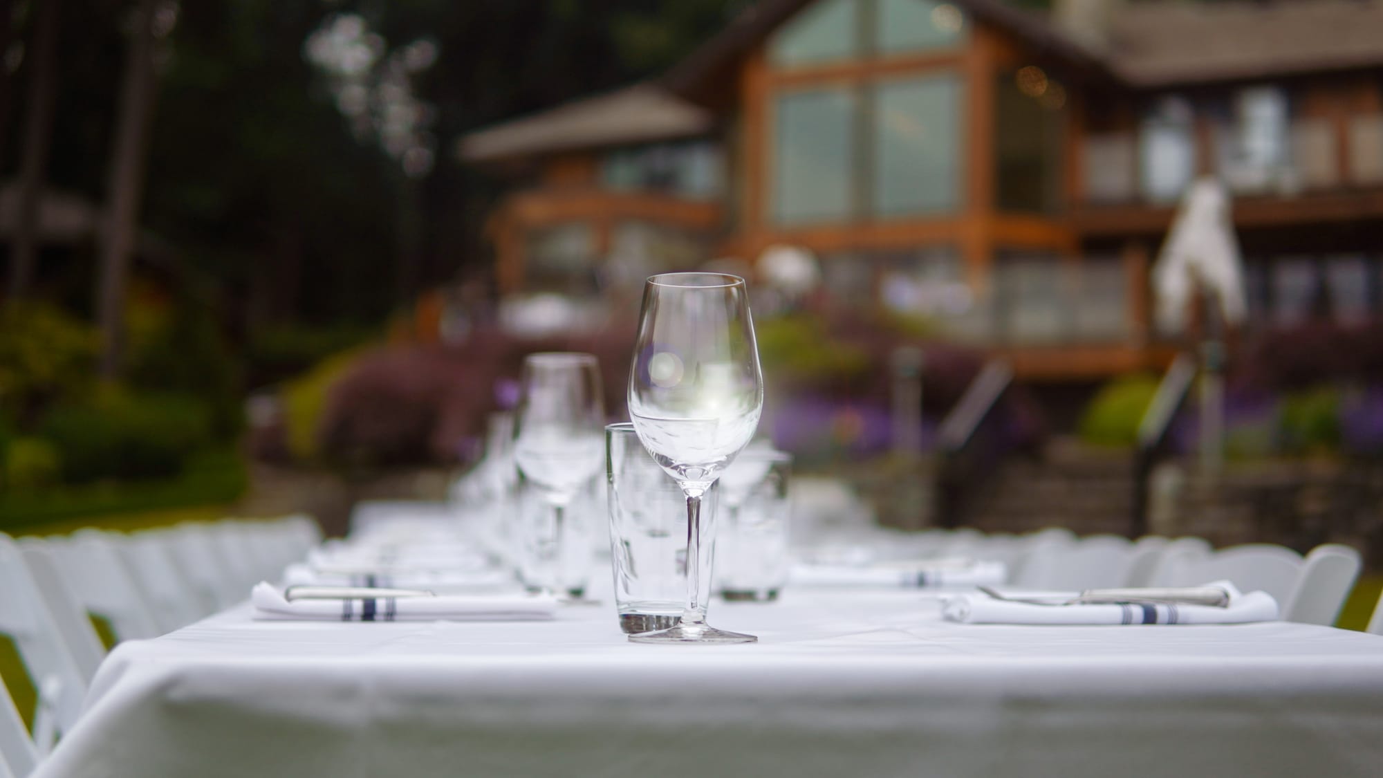 Wine glass on a dining table with the Lakeside House blurred behind