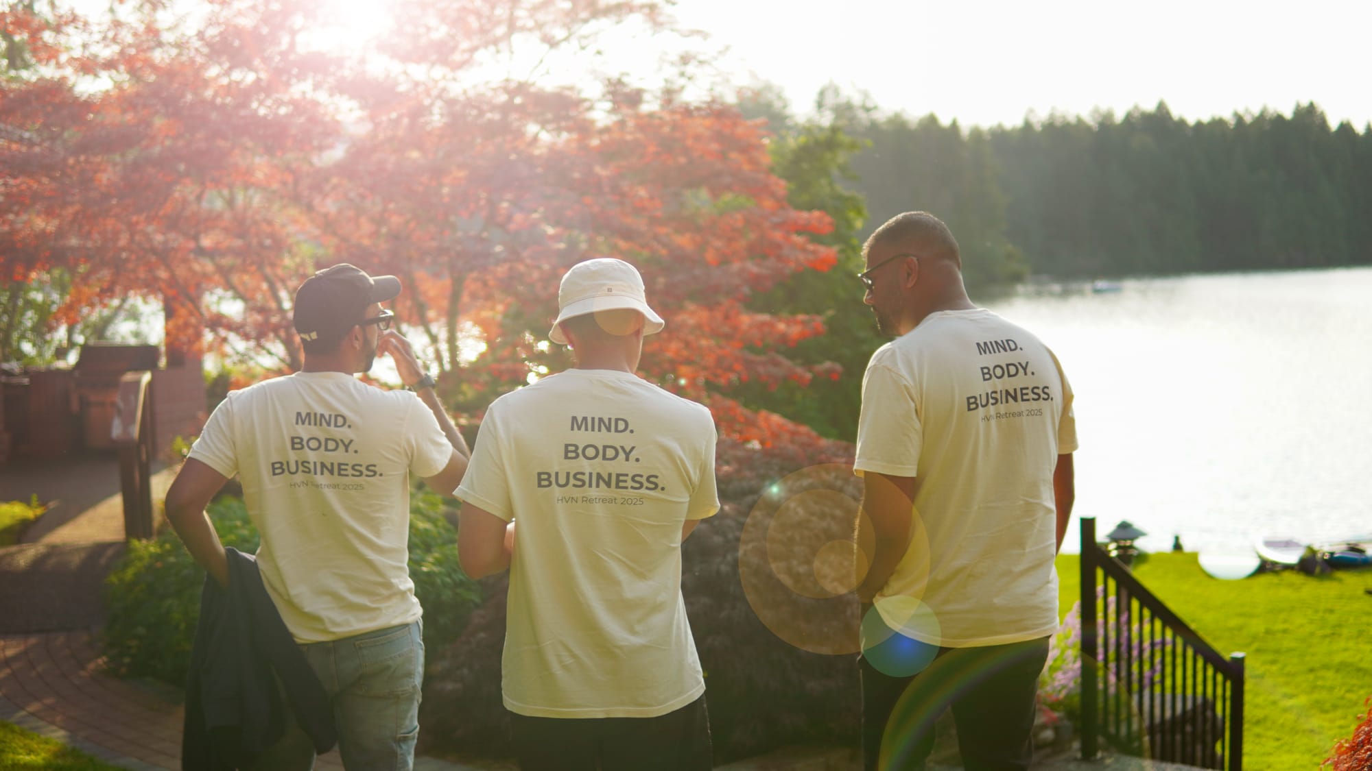 Three teammates in 'Mind. Body. Business.' shirts looking out over the lake at sunset